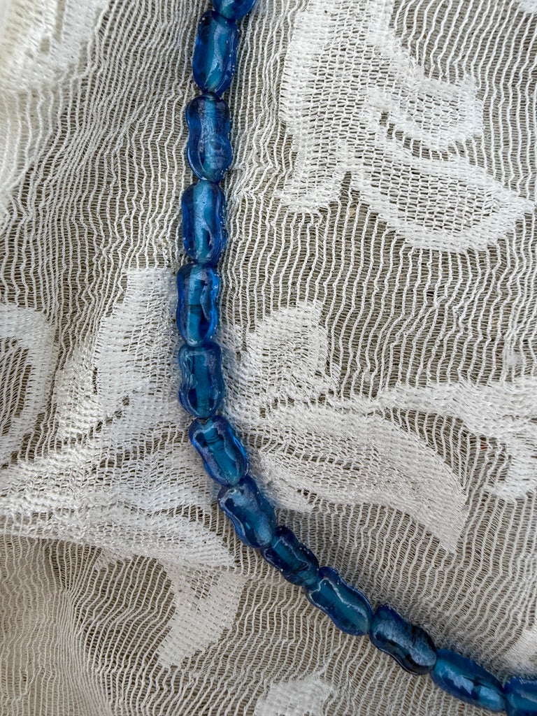 Blue beaded necklace on a textured white fabric background