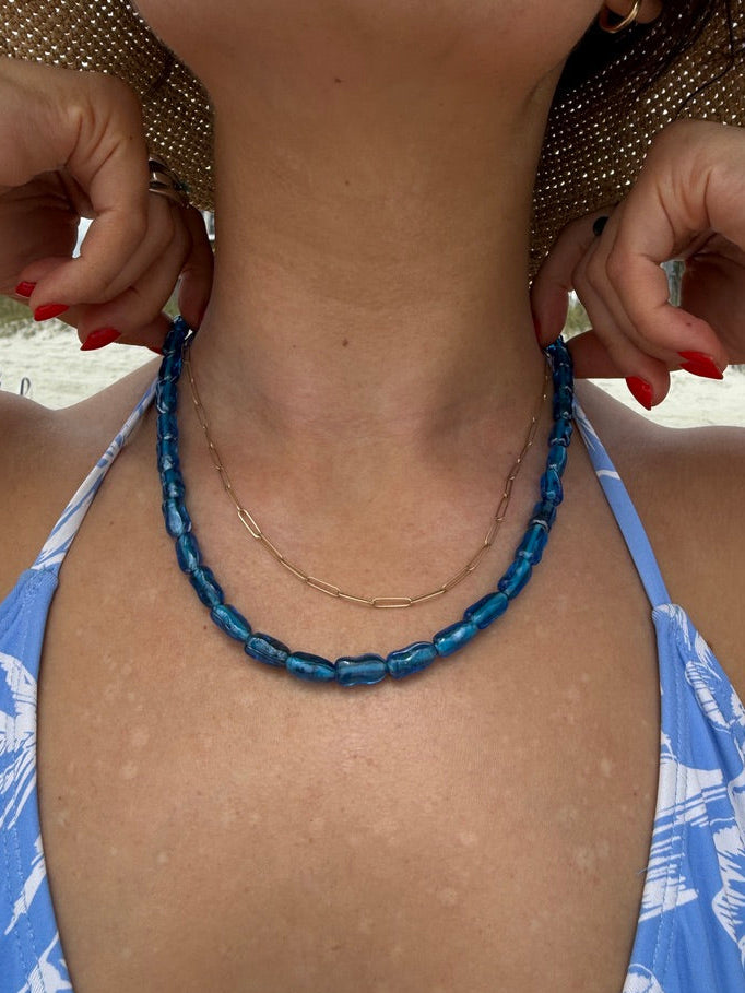Person wearing a blue beaded necklace with a blurred background