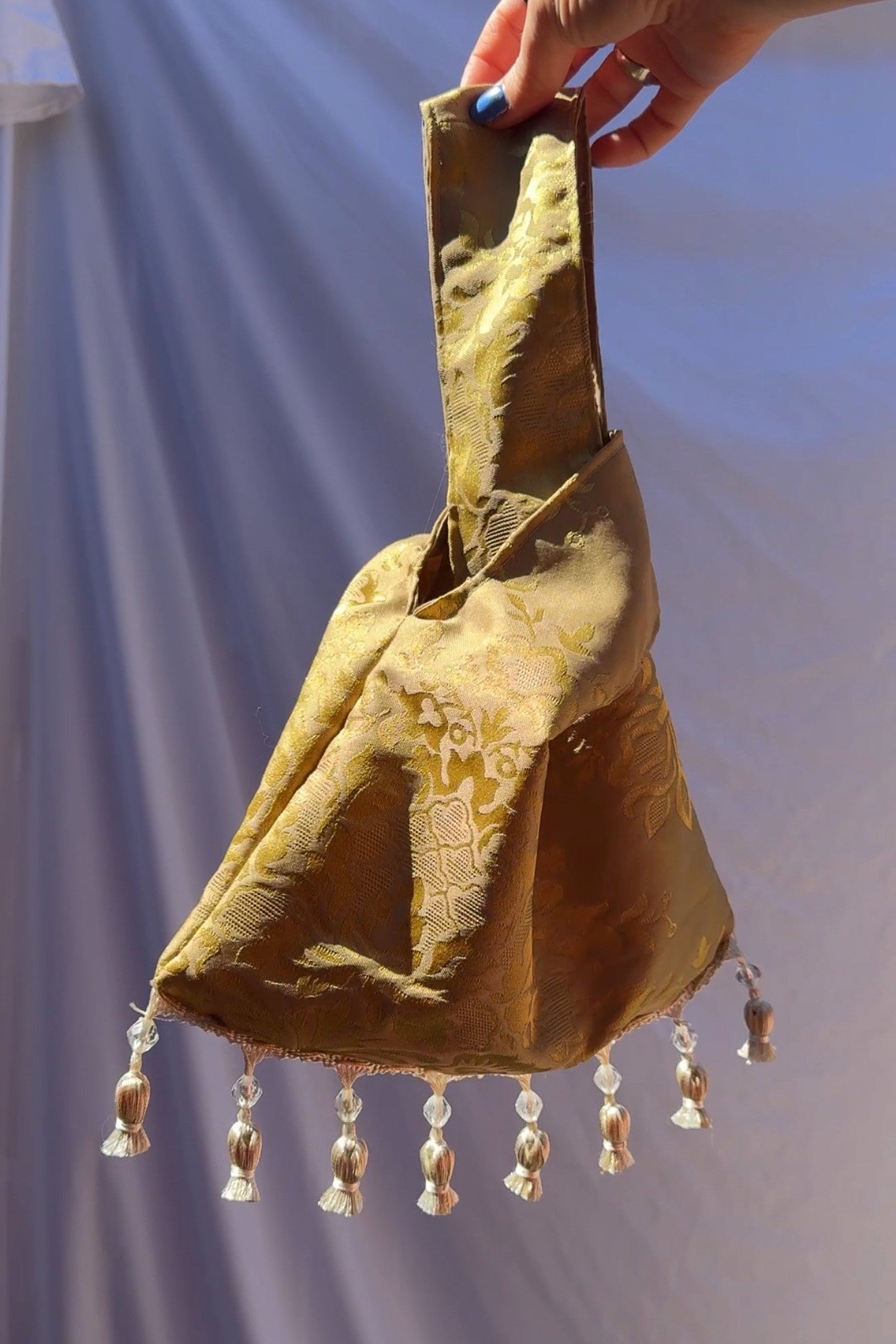 Hand holding a textured bag with tassels against a plain background