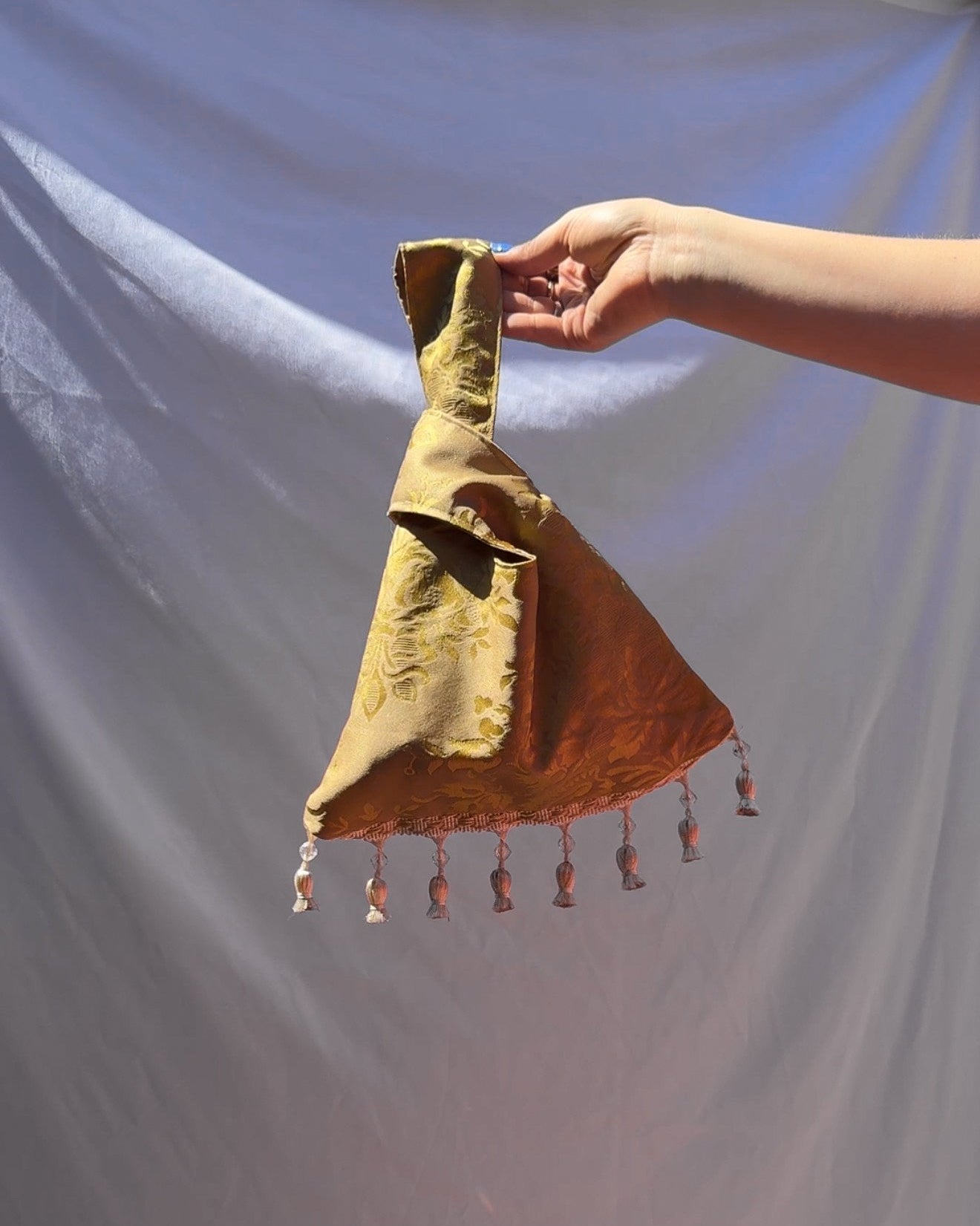 Hand holding a small, decorative bag with tassels against a plain background