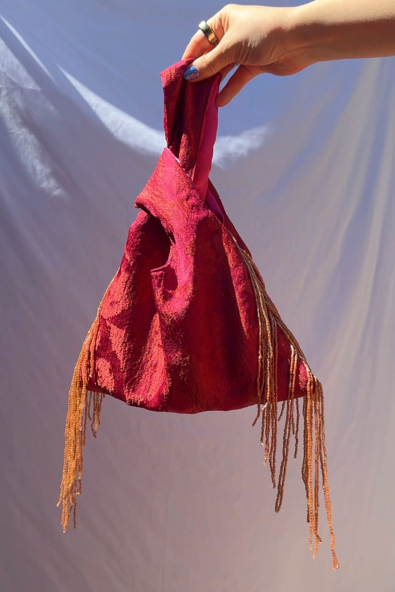 Red bag with fringes held by a hand against a plain background