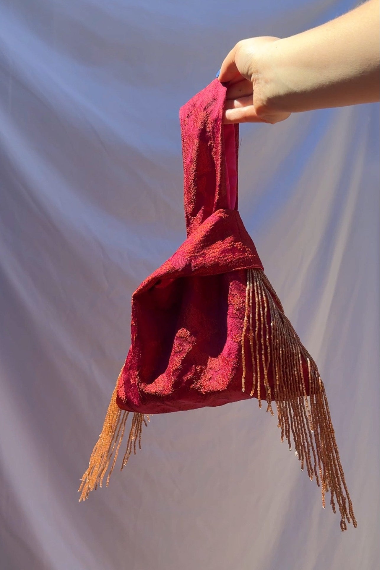 Red bag with fringes held by a hand against a plain background