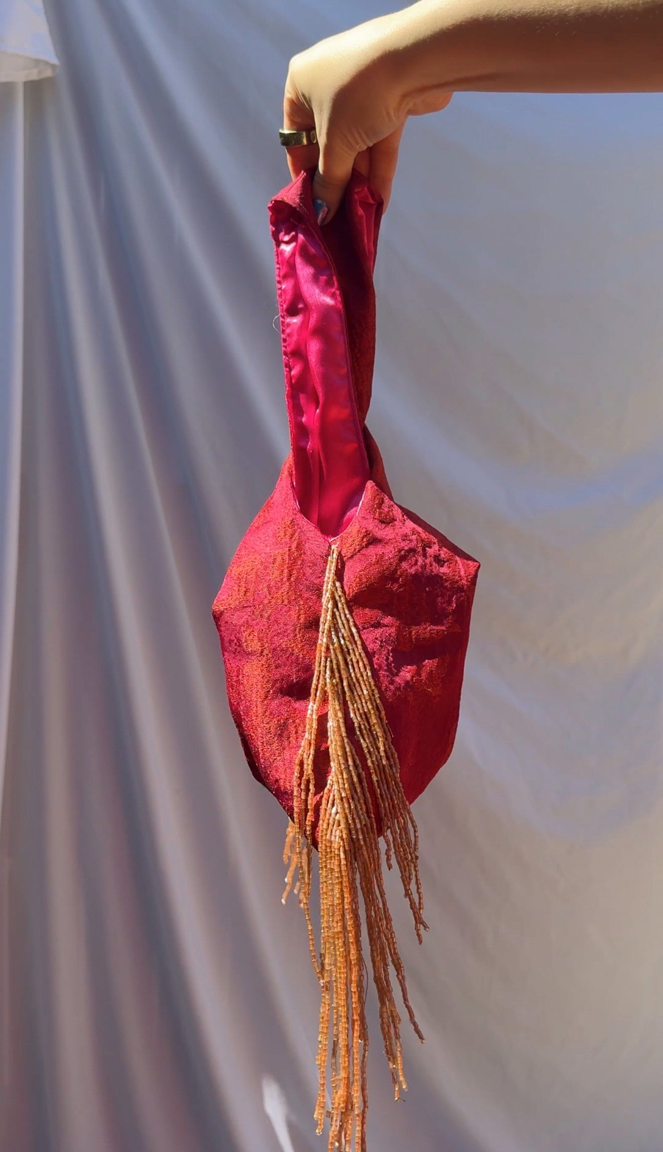 Fuchsia fabric naf with tassels held by a hand against a plain background